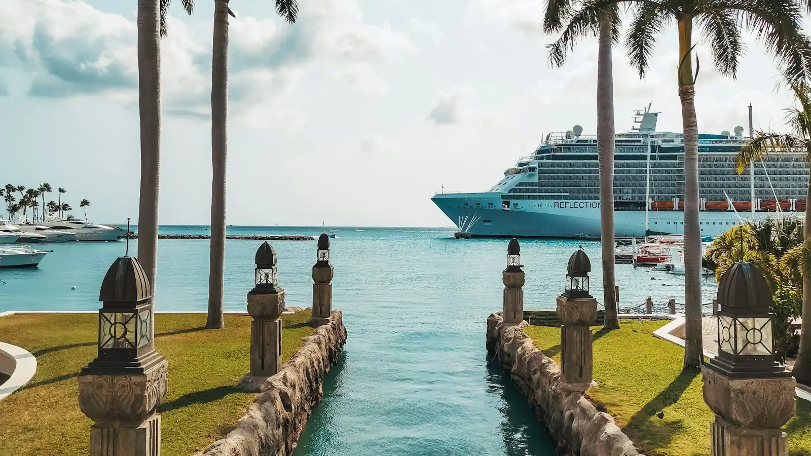 A cruise ship alongside a Caribbean pier seen past a line of palms on the shore