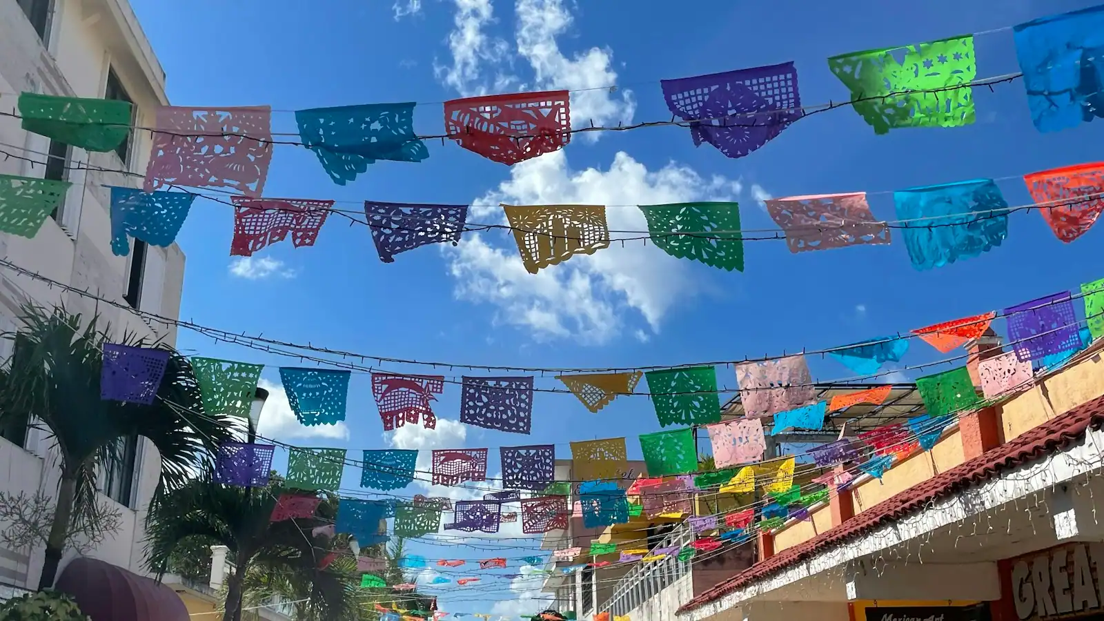A street strung with rows of coloured paper flags above low painted buildings in a Mexican town